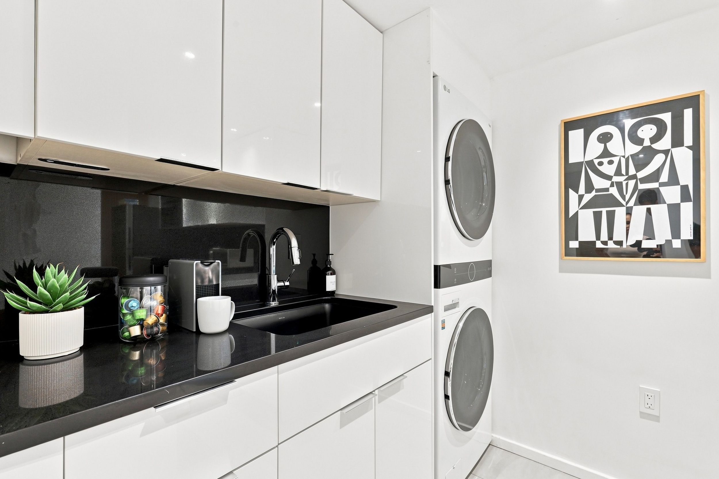 A modern kitchen with white cabinets, a black countertop, a sink, and a coffee machine.