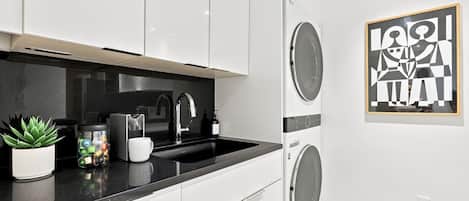 A modern kitchen with white cabinets, a black countertop, a sink, and a coffee machine.