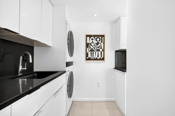 A modern kitchen with a black countertop, stainless steel appliances, and a wall-mounted artwork.