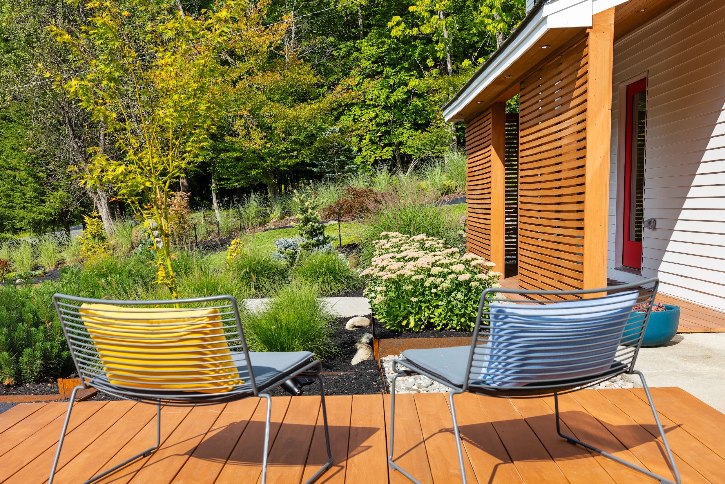 Une terrasse avec deux chaises, un petit jardin avec différentes plantes et un chalet en bois avec une porte rouge.