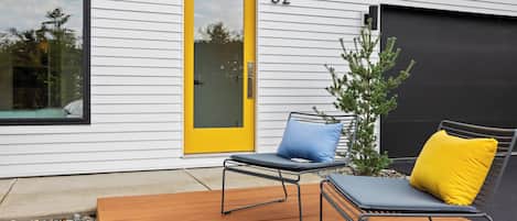 A modern house with a yellow door, numbered 32, and a deck with two lounge chairs and a small tree.