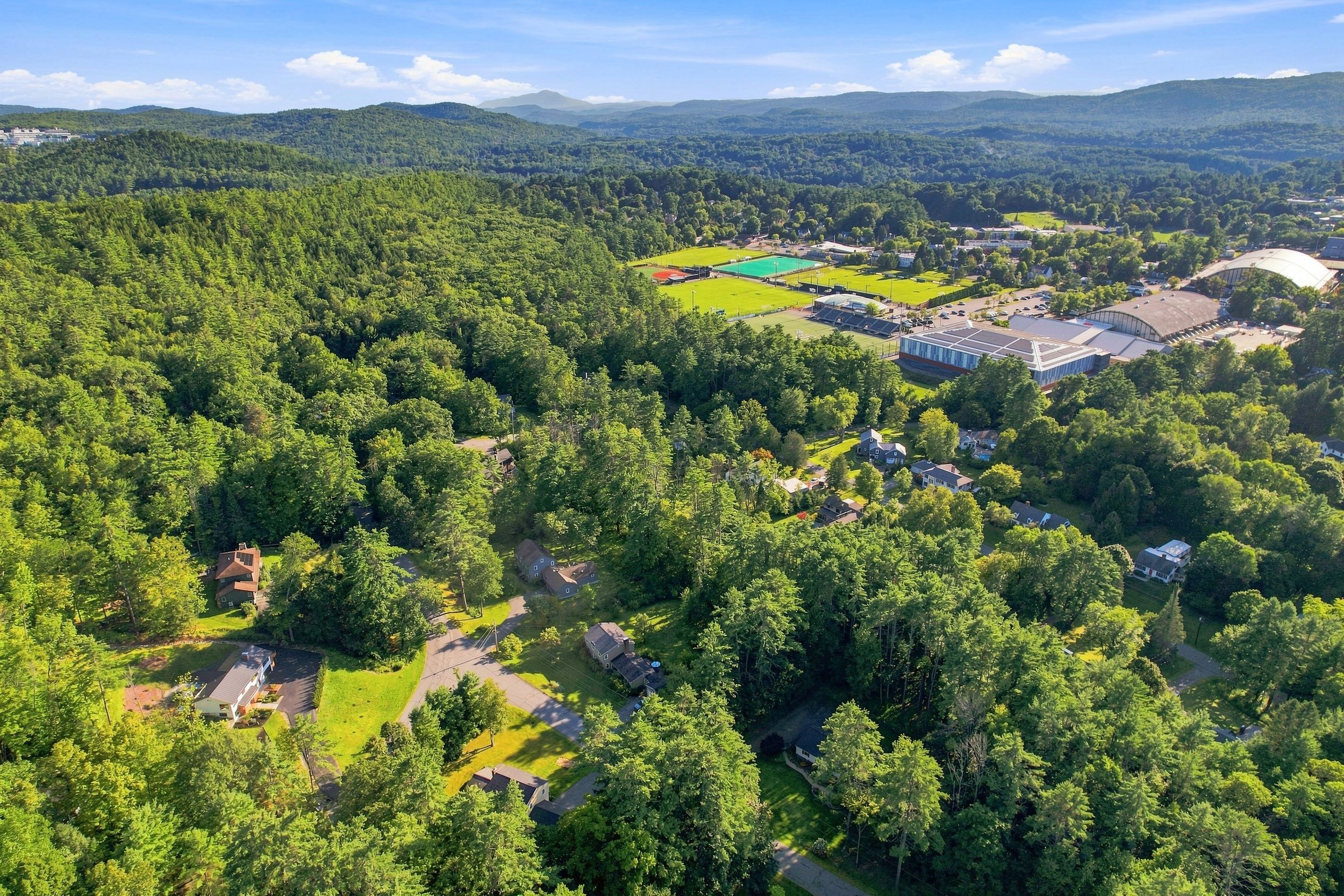 An aerial view of a residential area with multiple houses, a large sports field, and a stadium.