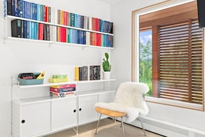 A room with a white bookshelf filled with books, a cactus plant, and a white furry chair. - Cozy 1BR Hanover Apartment | Walk to Dartmouth (Hanover)