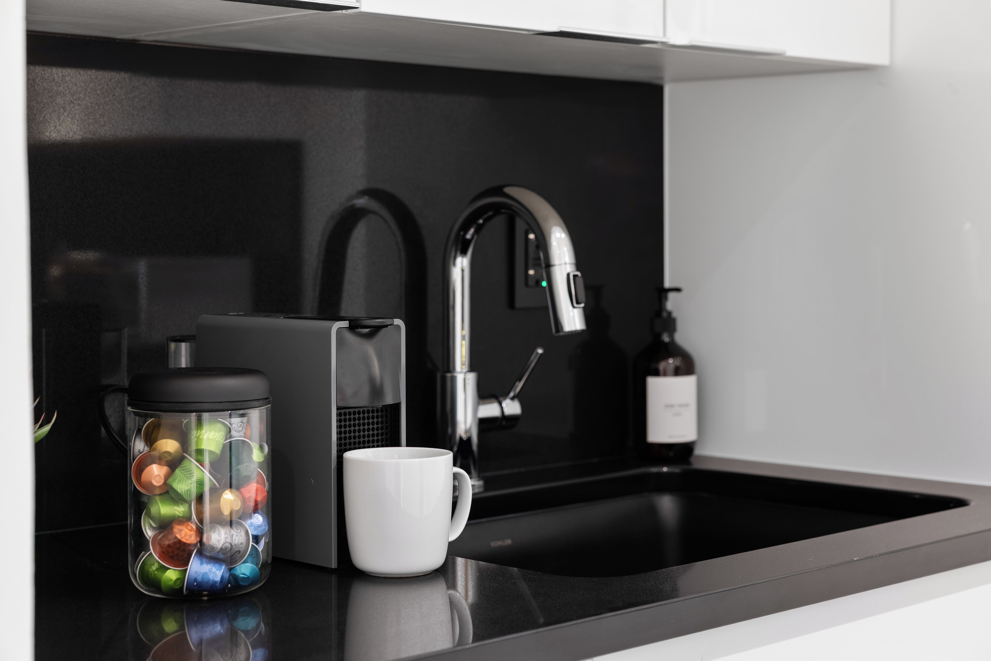 A modern kitchen with a black countertop, a coffee maker, a mug, and a bottle of hand soap.