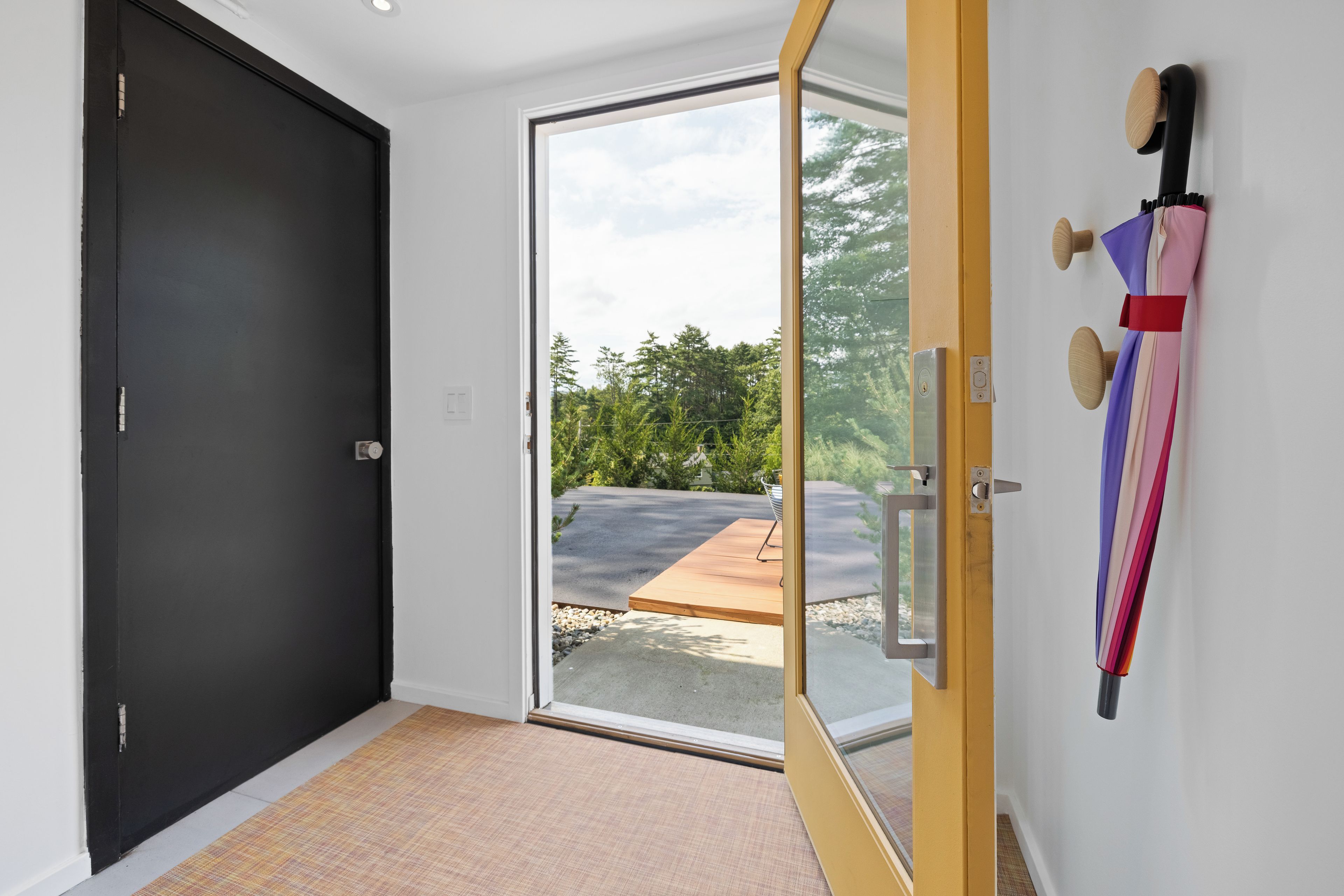 Un couloir avec une porte noire, une porte en verre donnant sur l’extérieur et une porte en bois avec une poignée en métal.