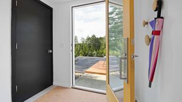 Un couloir avec une porte noire, une porte en verre donnant sur l’extérieur et une porte en bois avec une poignée en métal.
