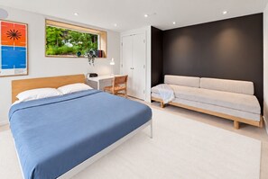 A bedroom with a bed, a desk, a chair, a sofa, and a window with a view of greenery. - Cozy 1BR Hanover Apartment | Walk to Dartmouth (Hanover)