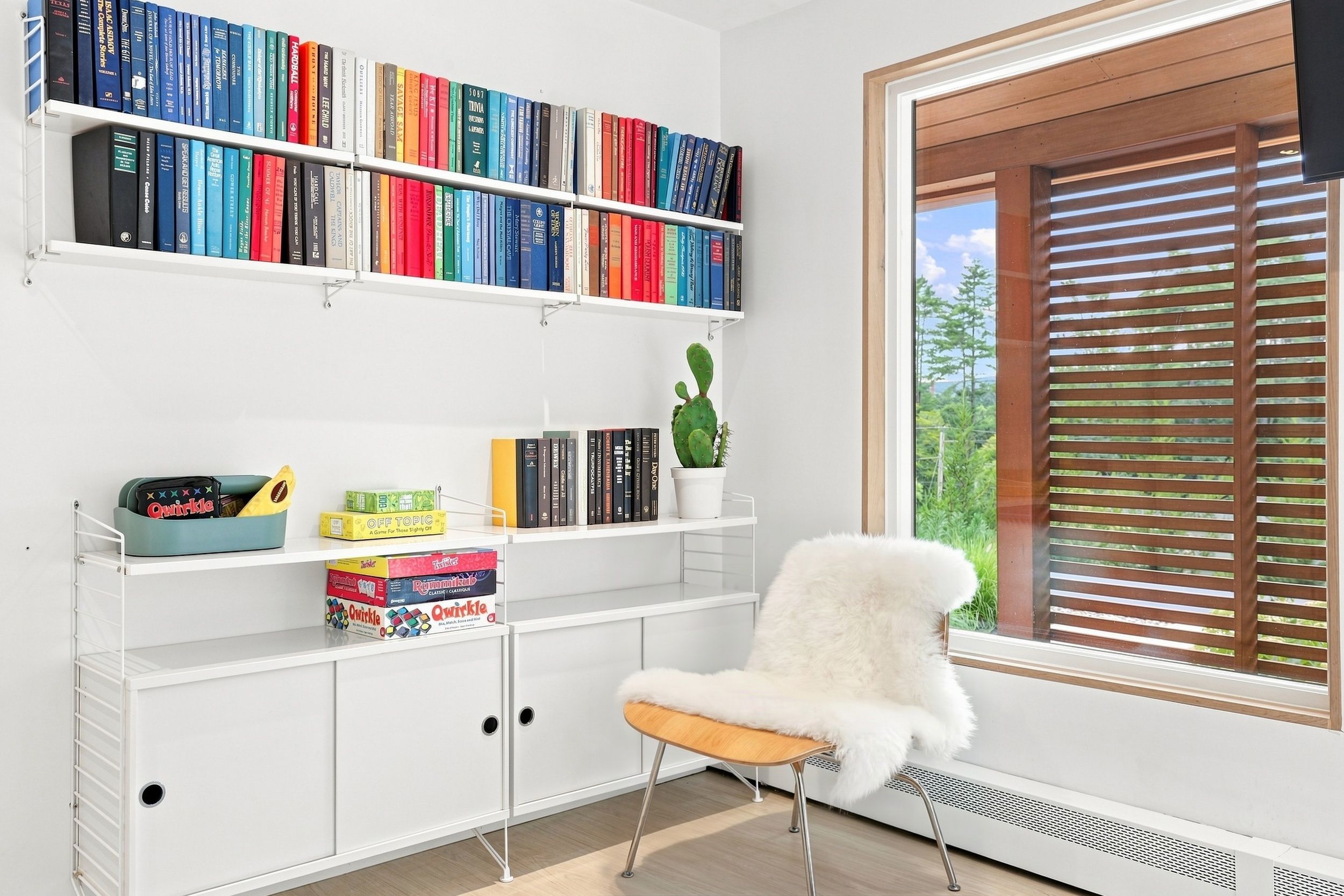 A modern room with a white bookshelf, a small white chair, and a window with wooden blinds.