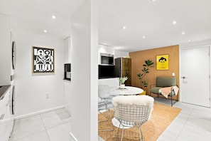 A modern kitchen with a built-in microwave, a dining area with a round table and wire chairs, and a living area with a sofa and a plant.
