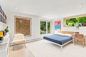 Un dormitorio moderno con cama, escritorio, silla y ventanas amplias.