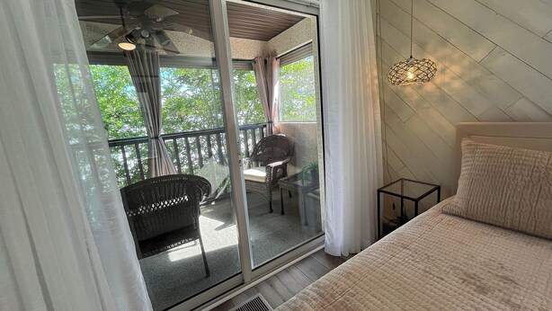 Una habitación con cama, una mesita, una silla, ventilador de techo y vista a un espacio exterior con una silla y una mesa.