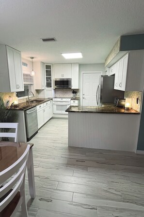 A modern kitchen with white cabinetry, a central island, and a dining area with a table and chairs. - 3-bedroom house short walk to beach with rooftop deck, putting green (St. Augustine)