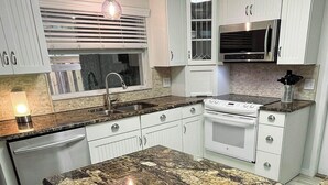 Una cocina con armarios blancos, horno de acero inoxidable, microondas y encimera de granito.