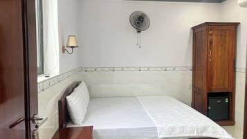 A bedroom with a bed, a bedside table, a wall-mounted fan, a cabinet, and a window with a curtain.