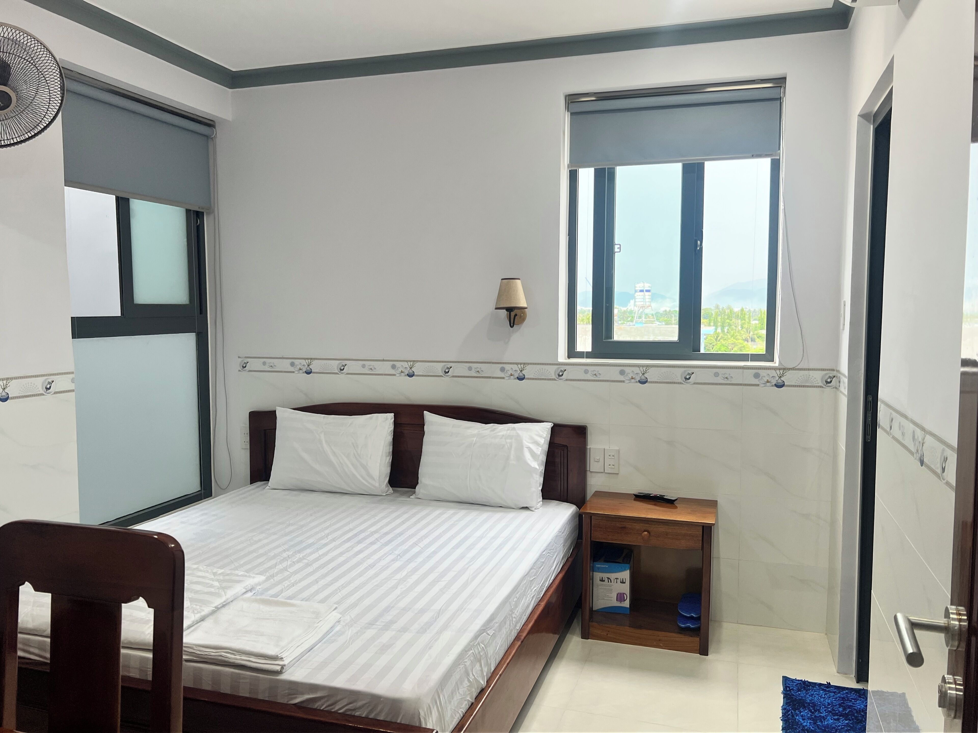 Ein Schlafzimmer mit Bett, Nachttisch, Fenster und einer Wandlampe.