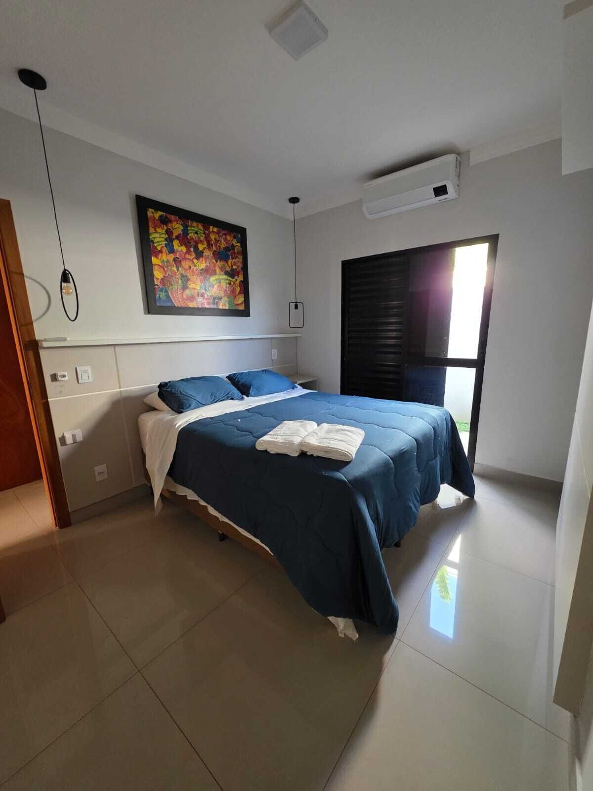 Un dormitorio con cama, un cuadro, un equipo de aire acondicionado y una ventana.