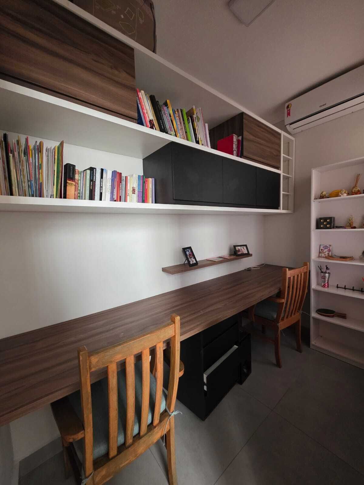 A study area with a wooden desk, chairs, bookshelves, and a white air conditioning unit.