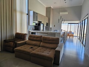 A modern living room with a sofa, a dining area with chairs, and a kitchen with cabinets.