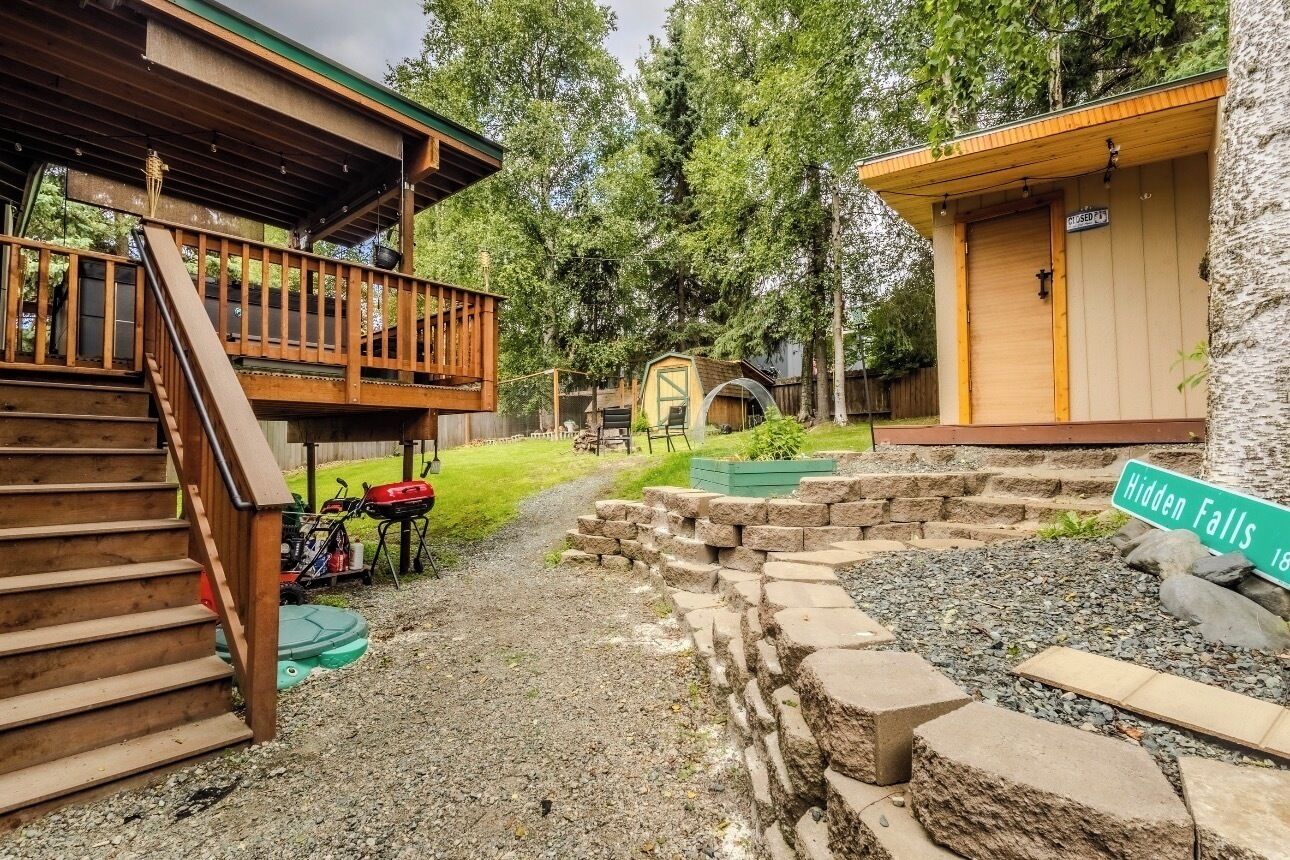 A cabin with a wooden deck, a covered porch, and a stone retaining wall.