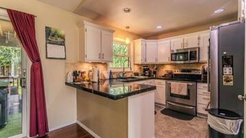 A kitchen with white cabinets, a granite countertop, stainless steel appliances, and a view through a glass door.
