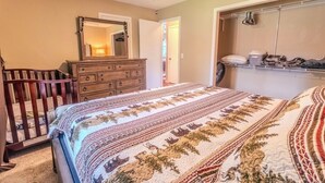 A bedroom with a crib, a dresser, a bed with a patterned bedspread, a ceiling fan, and a walk-in closet with shelves.