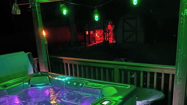 An outdoor hot tub with a wooden deck and a trash can.