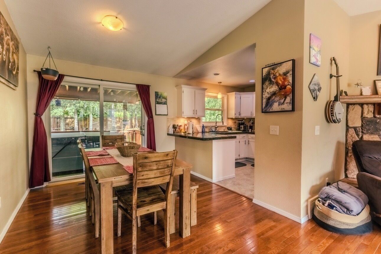 A dining area with a wooden table and chairs, a kitchen with white cabinets, and a living area with a couch and a guitar.