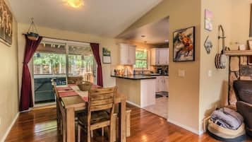 A dining area with a wooden table and chairs, a kitchen with white cabinets, and a living area with a couch and a guitar.