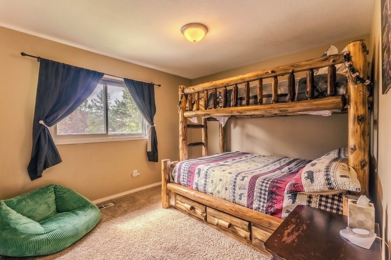 A bunk bed with a wooden frame, a green bean bag chair, a window with curtains, and a bedside table with a tissue box.