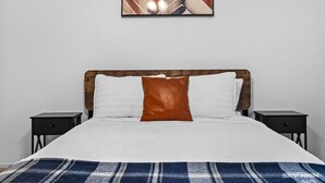 Una cama con cabecera de madera, almohadas blancas y marrones, una manta escocesa y dos mesitas de noche.