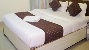 A hotel room with a bed, curtains, floral wallpaper, and an air conditioning unit.