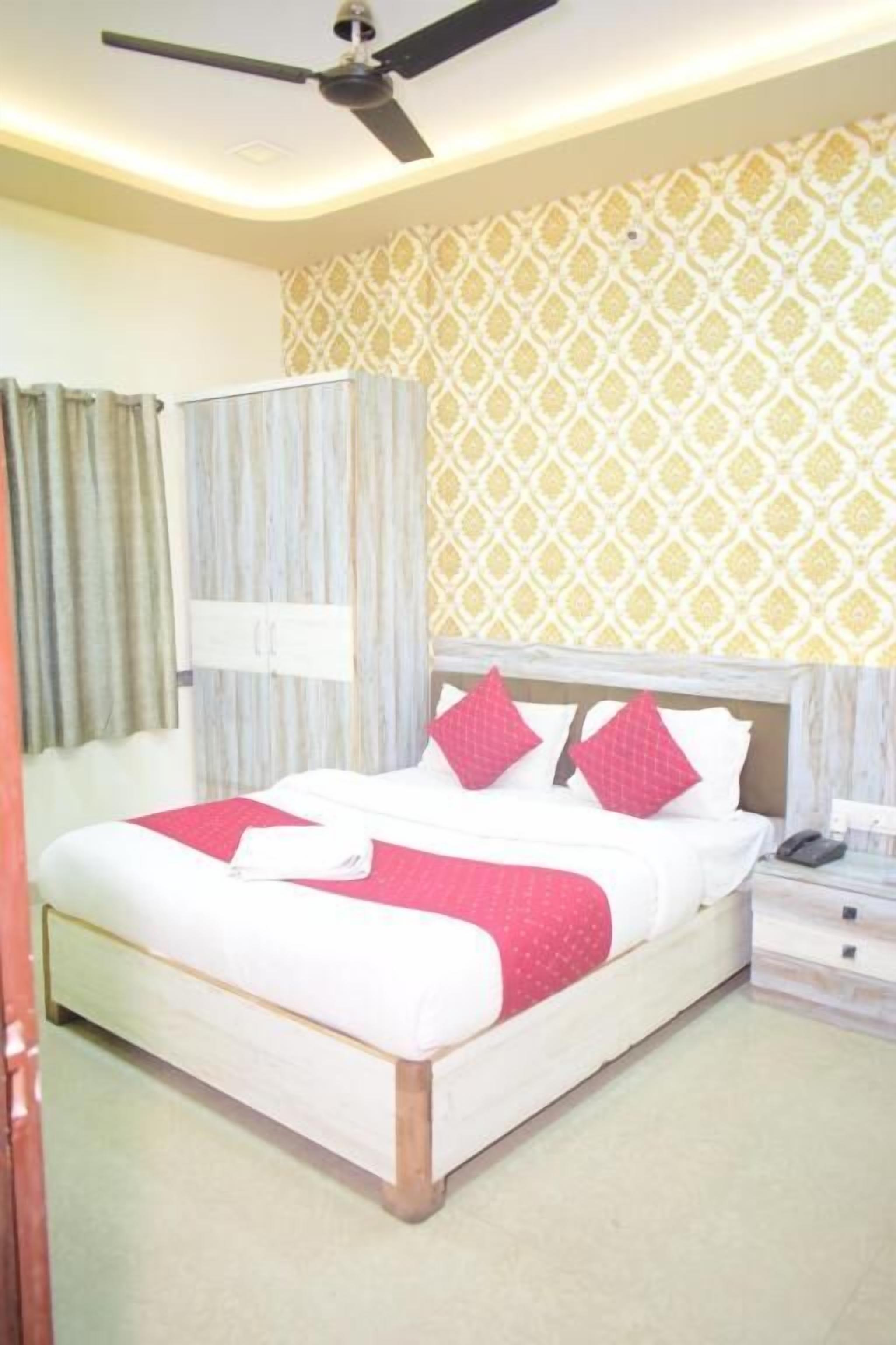 A bedroom with a bed, curtains, a ceiling fan, a bedside table, and a patterned wall.