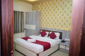 A bedroom with a bed, a nightstand, a wardrobe, and a patterned wall. - Hotel vinayak shree (Indore)