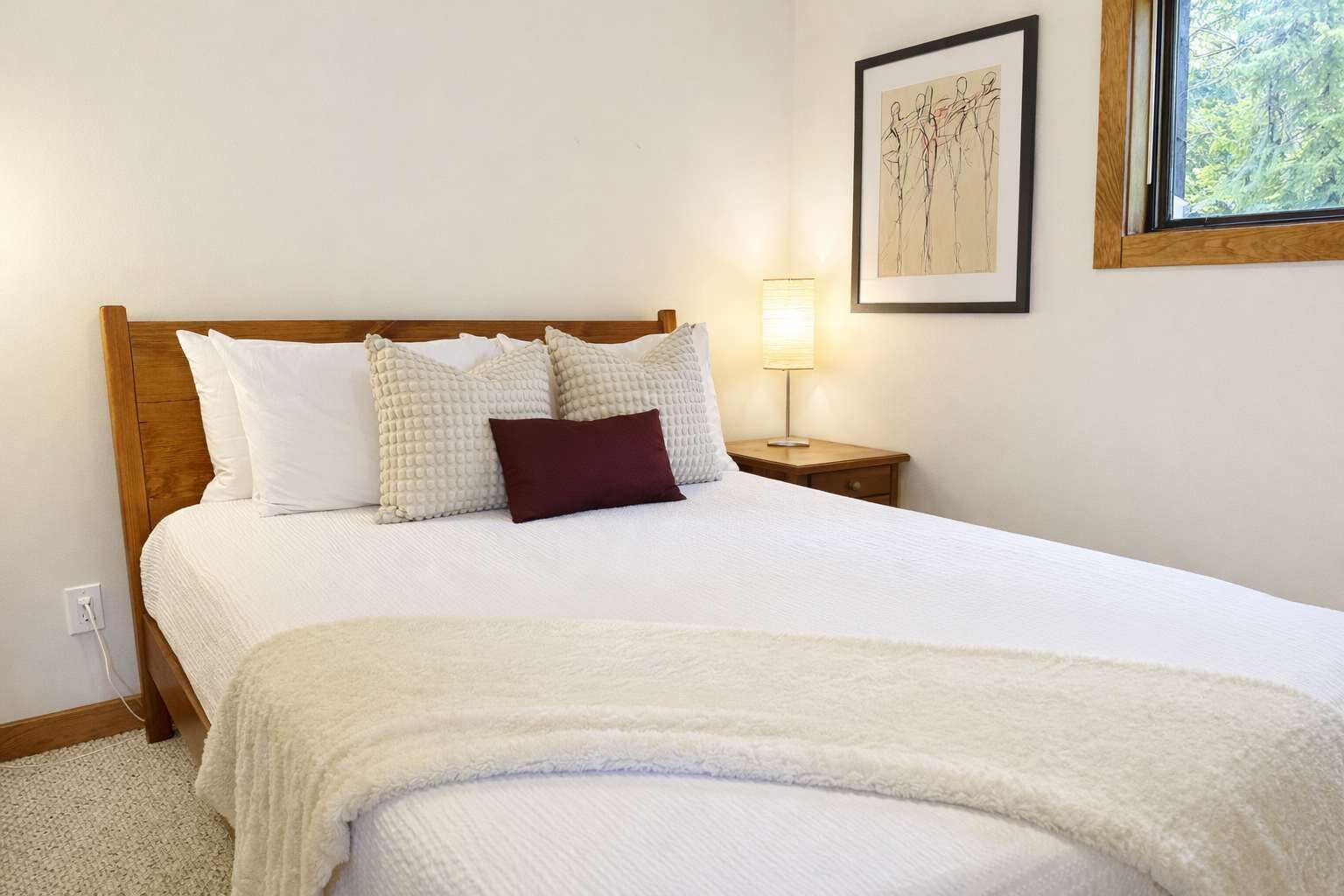 Un lit bien fait, avec une couette blanche et des oreillers, une tête de lit en bois, une lampe de chevet et une œuvre d’art encadrée accrochée au mur.