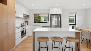 Eine moderne Küche mit weißen Schränken, einem Edelstahlkühlschrank, einer Holzeile mit Barhocker und Blick nach draußen durch ein Fenster.