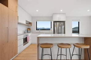 Eine moderne Küche mit Holzausstattung, einem Edelstahlkühlschrank, einem großen Fenster und einer Bar mit Hockern.