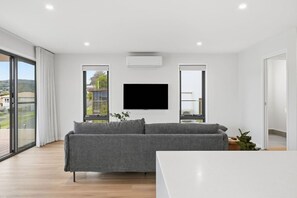 Ein modernes Wohnzimmer mit grauem Sofa, einem flachbildfernseher an der Wand und einer großen Glastür, die auf einen Balkon führt.