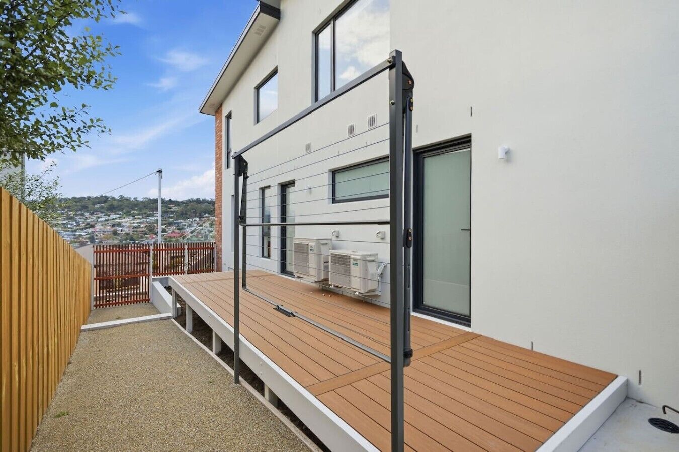 Un bâtiment moderne doté d’une terrasse en bois, de climatiseurs et offrant une vue sur un quartier résidentiel.