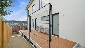 Un bâtiment moderne doté d’une terrasse en bois, de climatiseurs et offrant une vue sur un quartier résidentiel.