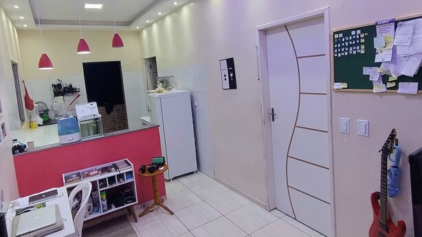 A modern kitchen with white cabinets, a red countertop, and a built-in oven. There is a small table with a laptop and headphones, and a red electric guitar hanging on the wall.