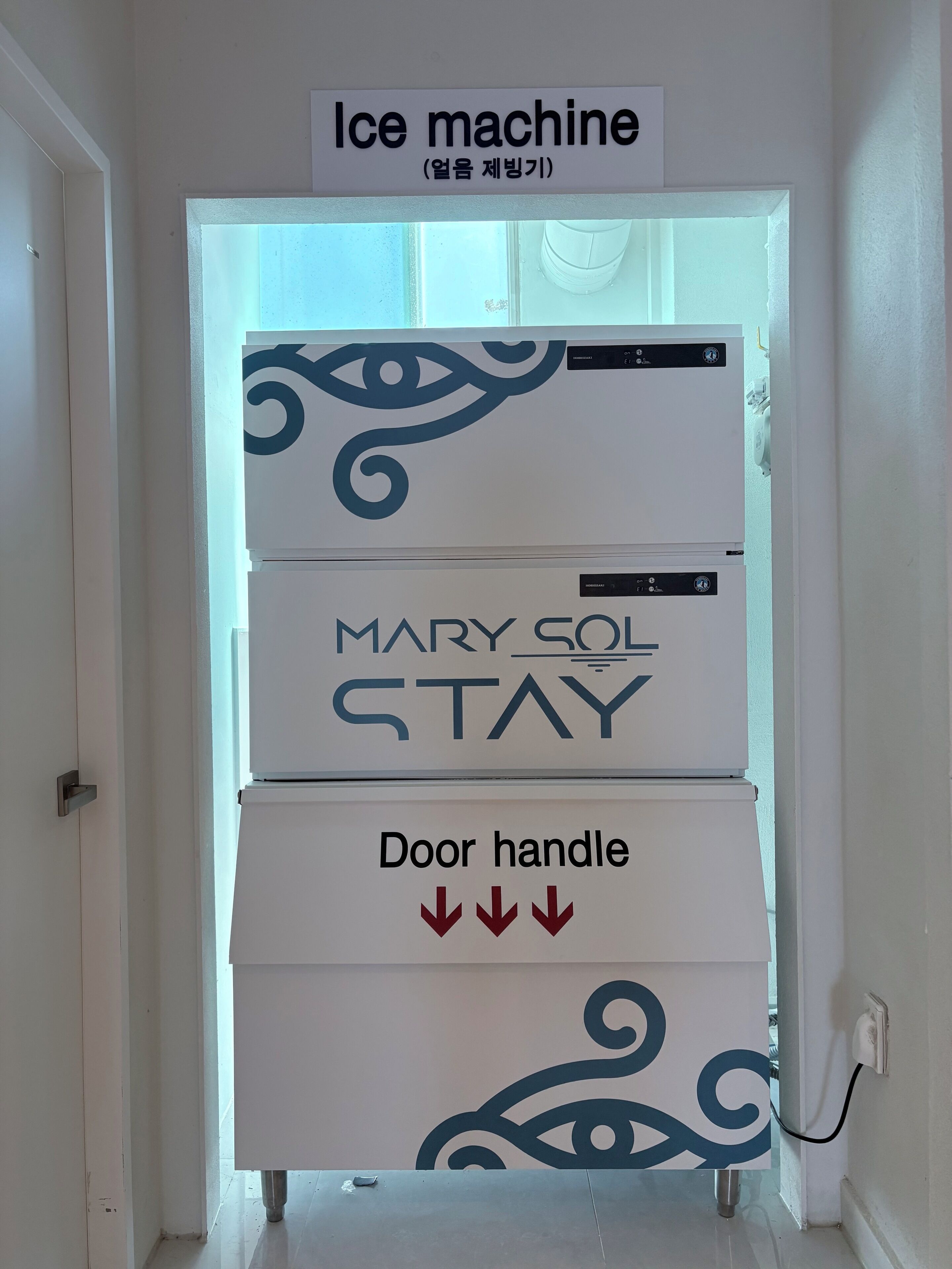 Una macchina per il ghiaccio con un cartello sopra che recita 'Mary Col Stay' e una maniglia della porta con frecce rivolte verso il basso.