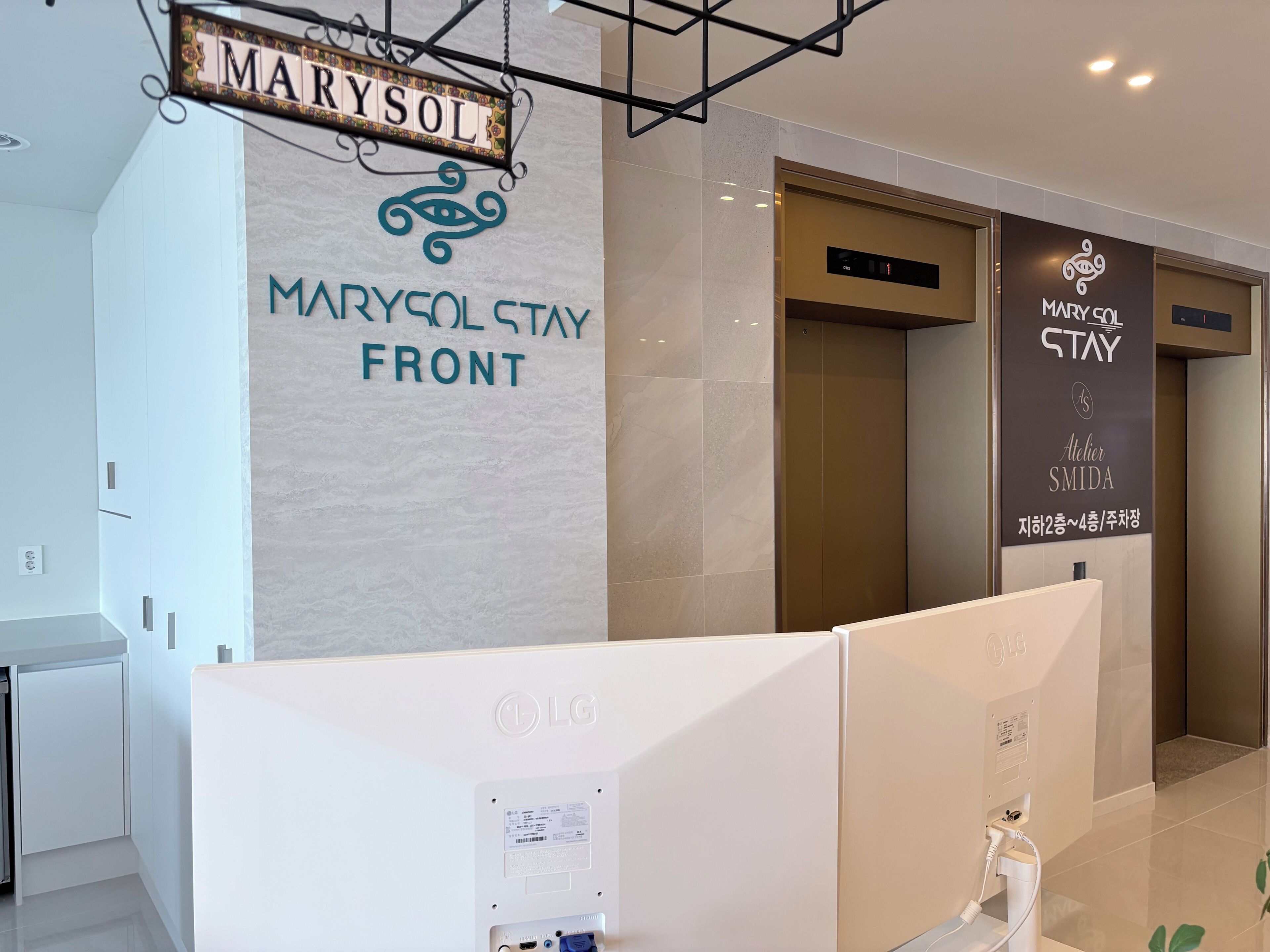 A reception area with a sign reading 'MARYSOL STAY FRONT' and an elevator with a sign 'MARYSOL STAY Atelier SMIDA.'