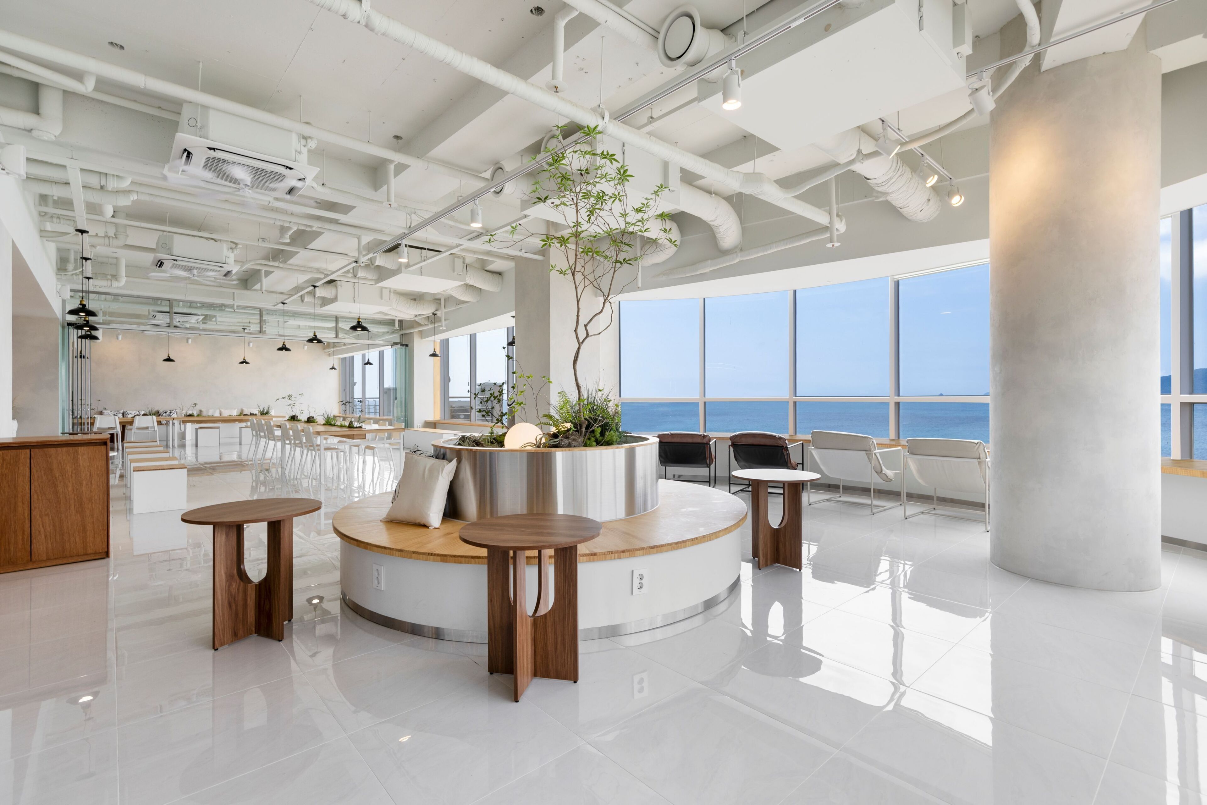 Ein modernes Interieur mit einer zentralen Sitzgruppe, großen Fenstern und Meerblick.