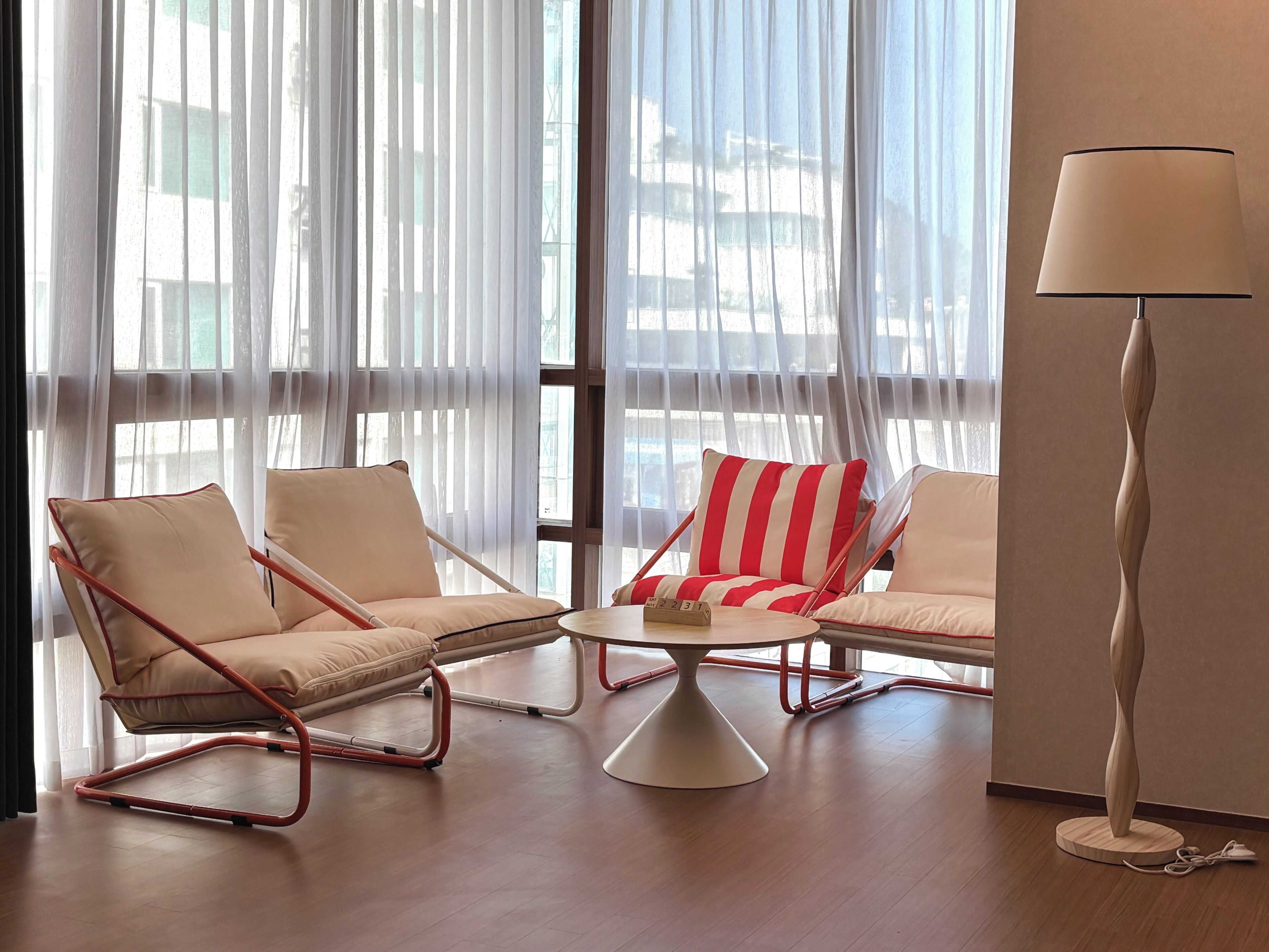 Une pièce comprenant deux fauteuils, une petite table ronde, une lampe et des rideaux légers.
