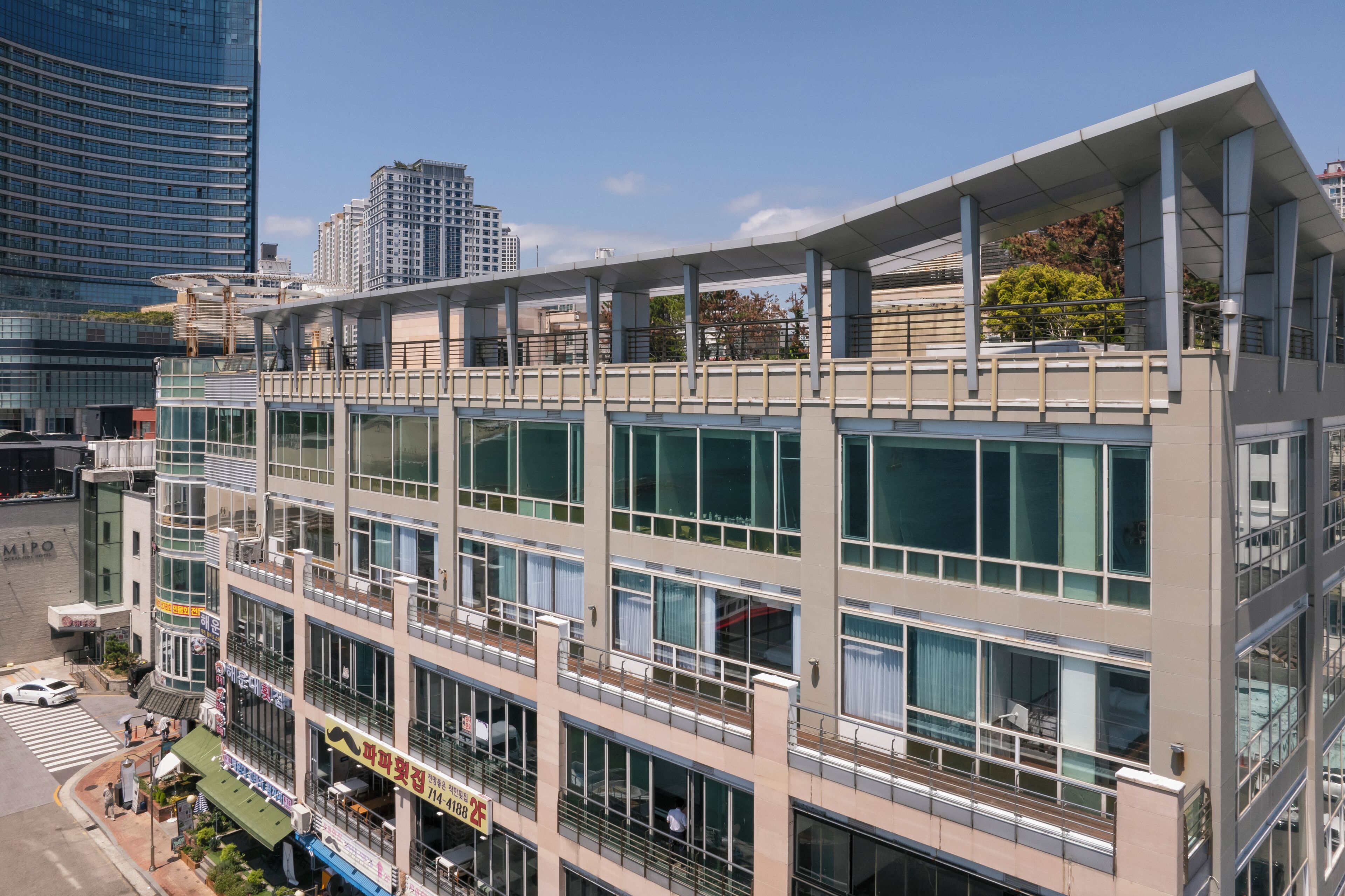 Un hotel de varios pisos con un diseño moderno, con balcones en los pisos superiores y un área comercial en la planta baja.