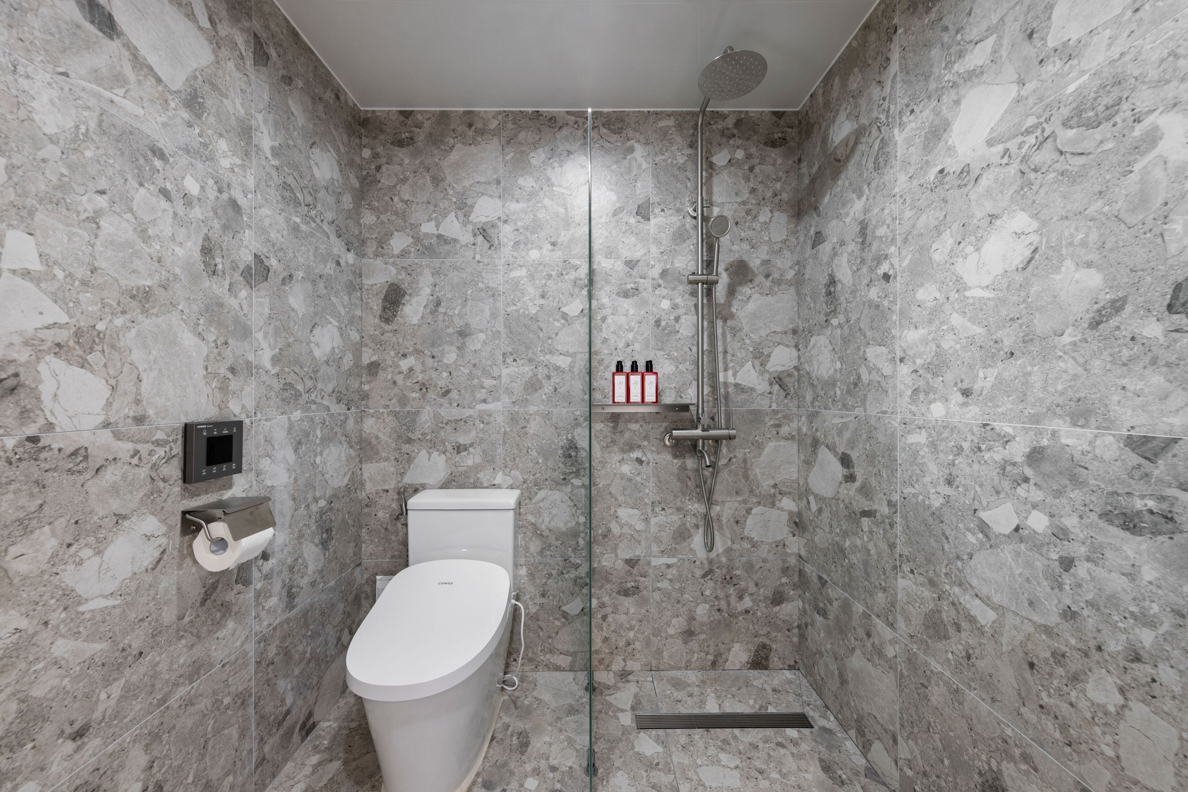 Une salle de bain moderne avec une douche à parois de verre, des toilettes et un mur en marbre.