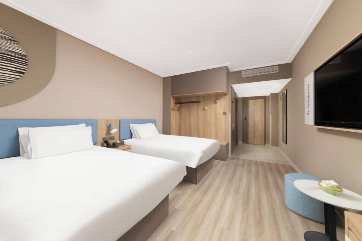 Una habitación de hotel con dos camas, una mesita, un televisor y un espejo.