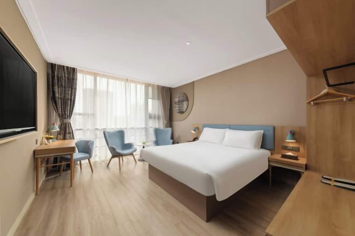 Habitación de hotel con cama, escritorio, dos sillas, televisor y ventana con cortinas.
