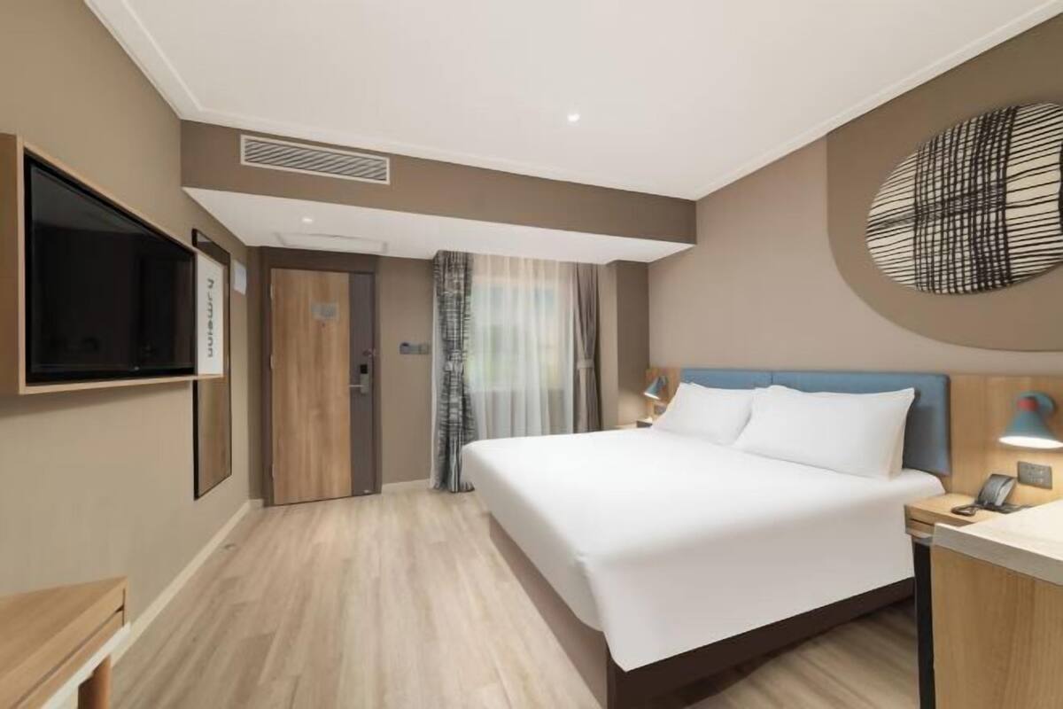 Habitación de hotel con cama, escritorio, televisor, puerta y ventana con cortinas.