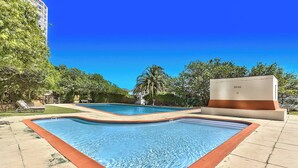 A swimming pool with a curved edge, surrounded by a tiled deck and a small building. - Table Mountain Escape, Mountain and sea Views (Cape Town)